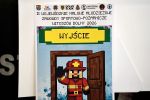 Plakat zawodów - przez drzwi wchodzi strażak pozdrawiający wszystkich podniesioną prawą ręką - plakat w stylizacji Minecraft
